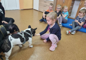 Uczennica karmi psa, w tle siedzą dzieci