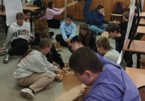 Grupa uczniów siedzi na podłodze podczas pracy warsztatowej