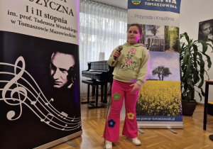Uczennica stoi z mikrofonem na tle banerów