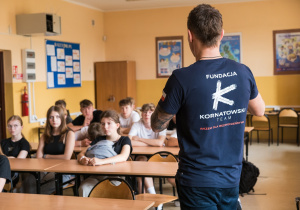 Uczniowie siedzą w ławkach i słuchają prowadzących zajęcia