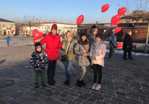 Troje uczniów stoi na placu z dwiema paniami trzymając balony w kształcie serca.