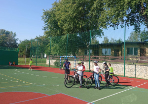 Sześcioro uczniów na rowerach przygotowuje się do konkurencji na boisku szkolnym.