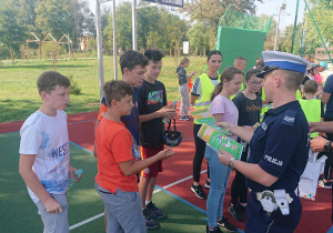 Dwóch policjantów wręcza dyplomy uczniom.