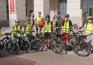 Sześcioro uczniów w kaskach, kamizelkach z rowerami oraz opiekunami stoją przed Urzędem Miasta.