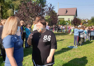 Uczniowie stoją z paniami na trawniku przed szkołą, wychowawczyni kl. I rozmawia z p.dyrektor..