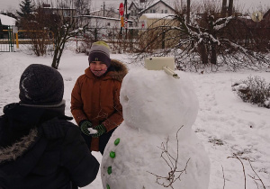 Dwóch uczniów stoi przy śnieżnym bałwanie.