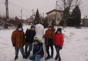 Czterech uczniów stoi przy ulepionym bałwanie, jeden uczę kuca przed nim.