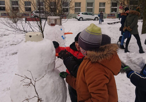 Dwóch uczniów dekoruje bałwana.