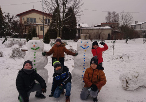 Dwóch uczniów stoi przy dwóch bałwanach, trzech chłopców kuca przed nimi.