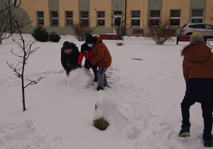 Trzech uczniów toczy śnieżną kulę.