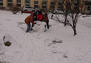 Pięciu uczniów toczy śnieżną kulę.