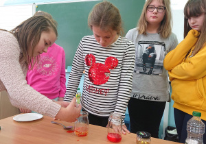 Cztery uczennice przyglądają się jak koleżanka wstrzykuje płyn do słoika.