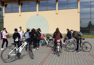 Grupa uczniów stoi z rowerami na parkingu szkolnym.