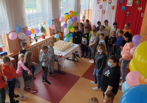 Uczniowie z nauczycielami stoją na korytarzu obok stolika na którym jest tort.