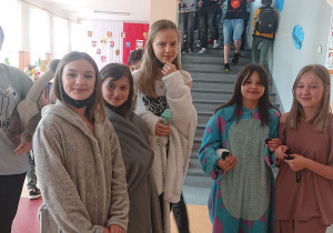 Uczniowie stoją w pidżamach szlafrokach na korytarzu szkolnym.