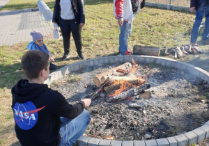 Cztery osoby stoją przy ognisku.