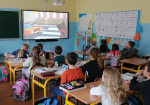 Grupa uczniów siedzi w ławkach i ogląda film.