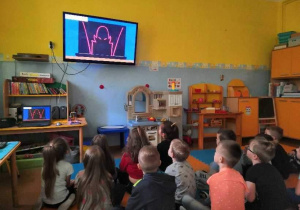 Grupa uczniów siedzi w ławkach i ogląda film.