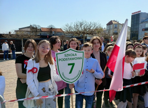 Grupa uczniów pozuje do zdjęcia z flagą oraz z tarczą szkoły.