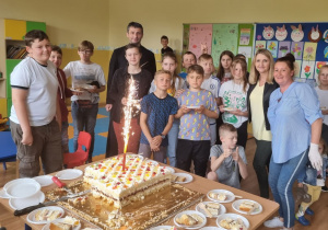 Uczniowie, p. dyrektor, przedstawiciel Rady Rodziców oraz ksiądz pozują do zdjęcia z tortem.