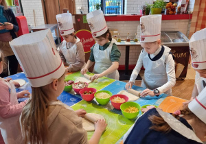 Uczniowie stoją przy stole i robią pizzę.