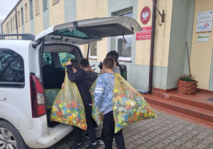 Czterech uczniów wkłada worki z nakrętkami do bagażnika samochodu.