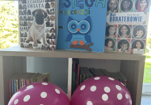 Regały z książkami w bibliotece szkolnej, fioletowe balony w białe kropki.