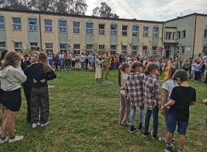 Grupa uczniów stoi przed budynkiem szkoły