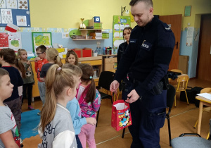 Pan dzielnicowy częstuje dzieci cukierkami na zakończenie spotkania