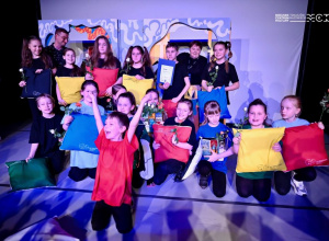 Dzieci w różnych pozach stoją na scenie i trzymają kolorowe poduszki