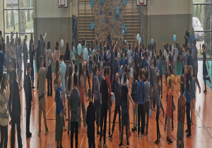 Uczniowie stoją na hali gimnastycznej z niebieskimi balonami