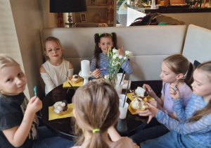 Kilka dziewczynek siedzi przy stoliku i je lody