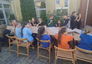 Uczniowie po występie jedzą pizze przy stolikach na zewnątrz
