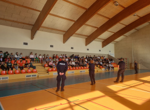 Uczniowie siedzą na hali sportowej i słuchają policjantów