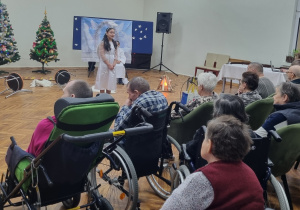 Grupa uczniów przedstawia jasełka, podopieczni z DPS siedzą na krzesłach i oglądają występ