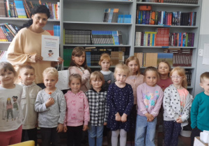 Dzieci stoją w bibliotece na tle półek z książkami