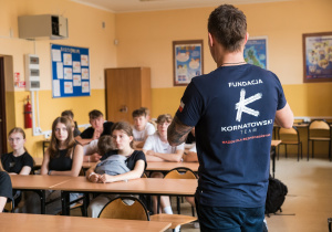 Uczniowie siedzą w ławkach i słuchają prowadzących zajęcia