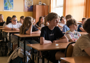 Uczniowie siedzą w ławkach i słuchają prowadzących zajęcia