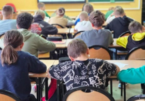 Uczniowie siedzą w ławkach i słuchają wykładu