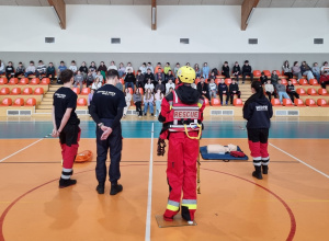 Pracownicy WOPR stoją na hali gimnastycznej w tle uczniowie