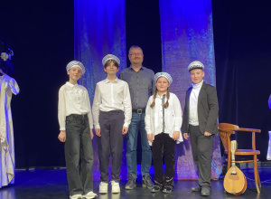 Uczniowie stoją na scenie z nauczycielem.