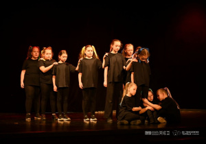 Dzieci w czarnych strojach prezentują scenę z przedstawienia