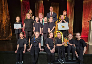 Dzieci w czarnych strojach stoją na scenie