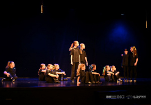 Dzieci prezentują scenę z przedstawienia siedząc i stojąc