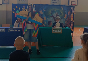 Uczniowie występują na scenie, na pierwszym planie uczennica przebrana za książkę
