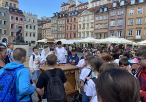 Uczniowie stoją przy katarynce i słuchają kataryniarza