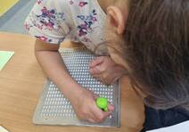Dziewczynka siedzi przy ławce i czyta alfabetem Braille’a
