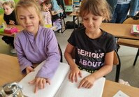 Dziewczynki siedzą przy ławce i czyta alfabetem Braille’a