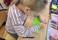 Dziewczynka siedzi przy ławce i czyta alfabetem Braille’a