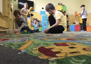 Dwóch uczniów bawi się na dywanie.